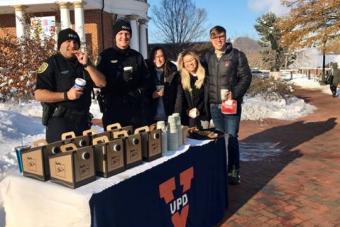 UVA police officers and students stand at a table with coffee containers and trays of cookies